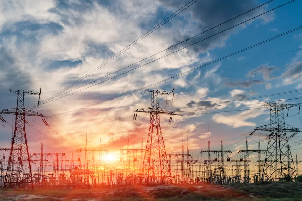 View of power towers at electric distribution substation against colorful sunset sky.